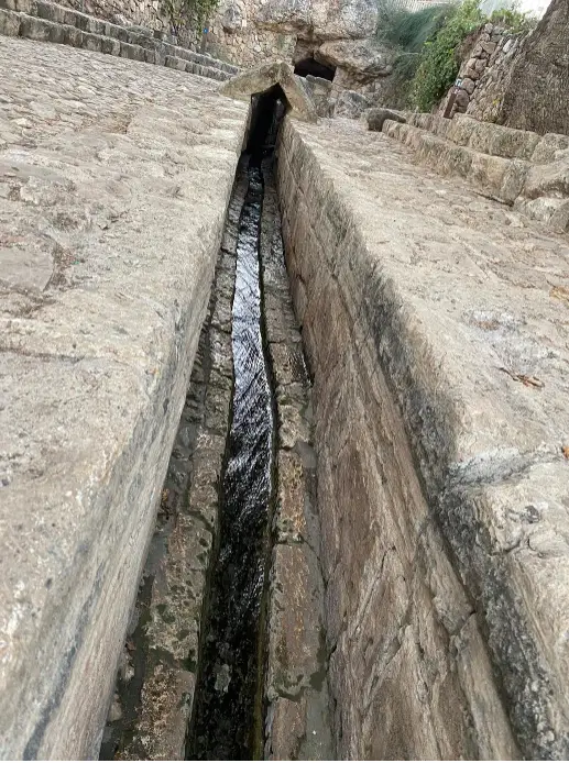 אמת מים צרה עם מים זורמים עוברת דרך מבנה אבן עתיק ומבולבל, ומציעה הצצה אל פלאי הטבע. פנינה נסתרת זו יכולה להיות ההרפתקה הבאה שלך, כפי שהומלץ בבלוג טיולים בארץ לחוות חוויות בטבע בישראל.