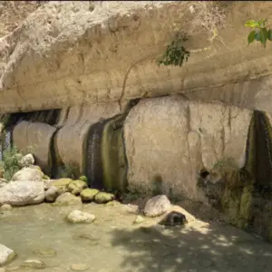מפל שליו זורם על צוק סלעי לתוך בריכה צלולה למטה, מציע חוויות בטבע בישראל קסום. אזוב וצמחים קטנים מוסיפים ירק לאבנים, בעוד סלעים גדולים מפוזרים מנצנצים תחת אור שמש עדין.