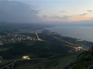 נוף בין ערביים מגבעה המשקיפה על עיירה מוארת, מושלם למטיילים החוקרים את ישראל. רשת של רחובות ושדות שמסביב מובילים לגוף מים עצום המשתרע אל האופק. השמיים עוברים מיום ללילה, עם עננים פזורים וגוני שקיעה - באמת אטרקציה ששווה לבקר בה.