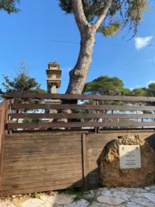 מגדל תצפית גבוה מעץ מתנשא מאחורי גדר, מוסתר חלקית על ידי עץ גדול. בחזית מונחת ליד הגדר אבן עם לוח הנצחה. השמיים הכחולים והצלולים קובעים את הסצנה לבלוג טיולים בארץ המציג מקומות מומלצים לטיול, מושלם לטיולים בצפון הארץ.