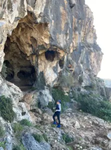 אדם חובש זקט וכיפה כחול חוקר כניסה למערה מחוספסת בצפון ההר של ישראל, שם מציעים טיולים בצפון הארץ אטרקציות מרתקות בין משטחי אבן מחוספסים וירק דליל. מושלם עבור כל בלוג טיולים בארץ המתעד בריחות הרפתקניות.