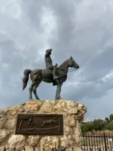 על רקע שמים מעוננים, הפסל הכובש הזה של רוכב על סוס על גבי דום אבן הוא אחד מאתרי הטיול שחובה לראות. הכן מציג תבליט עם סוסים בתנועה, בעוד שגדר מתכת וירק שופע מעטרים את הרקע, ומציעים למבקרים חוויה בלתי נשכחת.