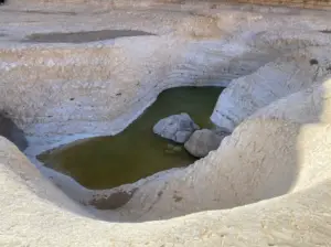 בריכה קטנה ורדודה עם מים ירקרקים מוקפת בתצורות גיר לבנות ונשחקות. סלעים גדולים שקועים חלקית במים, והנוף נראה יבש ומחוספס - מושלם למטיילים בישראל לחקור טיולים בצפון הארץ.