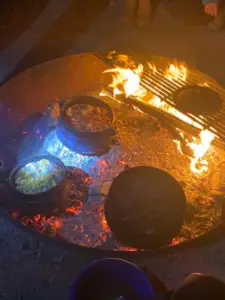 סירים מתבשלים על מדורה פתוחה עם להבות וגחלים זוהרות לוכדים את המהות של חוויות בטבע בישראל. סיר אחד, אולי מכיל אורז, מתבשל בעוד שאחרים יושבים על מגררת או ישירות על גחלים. נראה שהסצינה החיצונית הנעימה הזו מתפתחת במהלך טיול קמפינג בלתי נשכח.