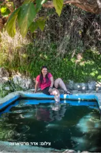 בבלוג האחרון שלה בארץ, אישה בחולצה ורודה ומכנסיים קצרים יושבת מחייכת למצלמה, טובלת את רגליה בבריכה חיצונית קטנה. מוקפת בירק השופע ובאור השמש של אחד הטיולים האהובים עליה בצפון הארץ, היא לוכדת את שמחת חוויות בטבע בישראל.