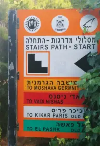 שלט הכוונה רב לשוני על שביל שופע מכוון את הדרך למטיילים בישראל למושבה גרמנית, ואדי ניסנאס, כיכר פריז ואל פאשה. הוא כולל סמלים, כולל לוגו וחצים, המנחים את המחפשים חוויות בטבע בישראל.