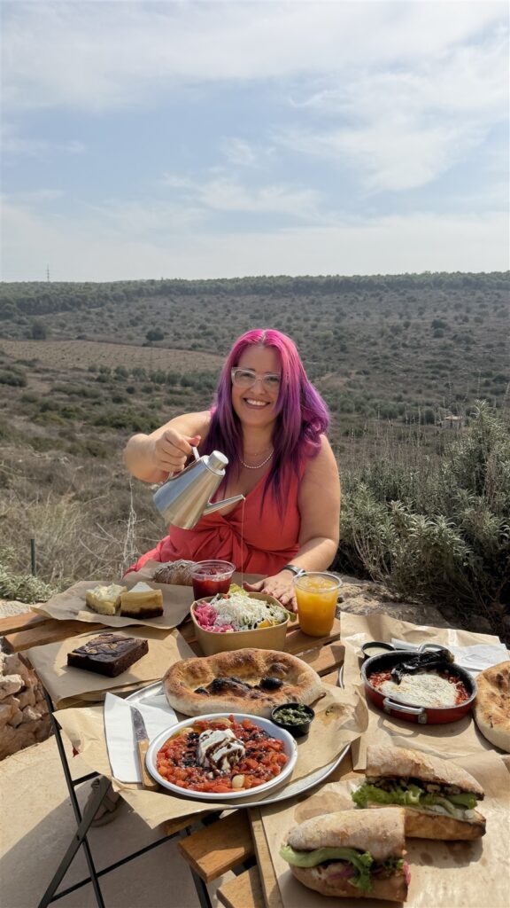אבנית יושבת ליד שולחן אוכל מול נוף מטעי זיתים